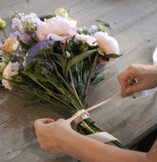 En person binder ett band runt en bukett med blommor på ett bord.